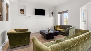 Una sala de estar con sofá, sillones, una mesa de centro y un televisor de pantalla plana montado en la pared.