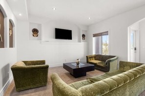 Ein Wohnzimmer mit einer Couch, Sesseln, einem Couchtisch und einem an der Wand befestigten Flachbildfernseher.