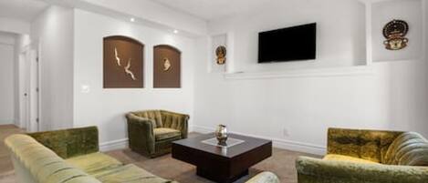 A living room with a sofa, armchairs, a coffee table, and a flat-screen TV mounted on the wall.