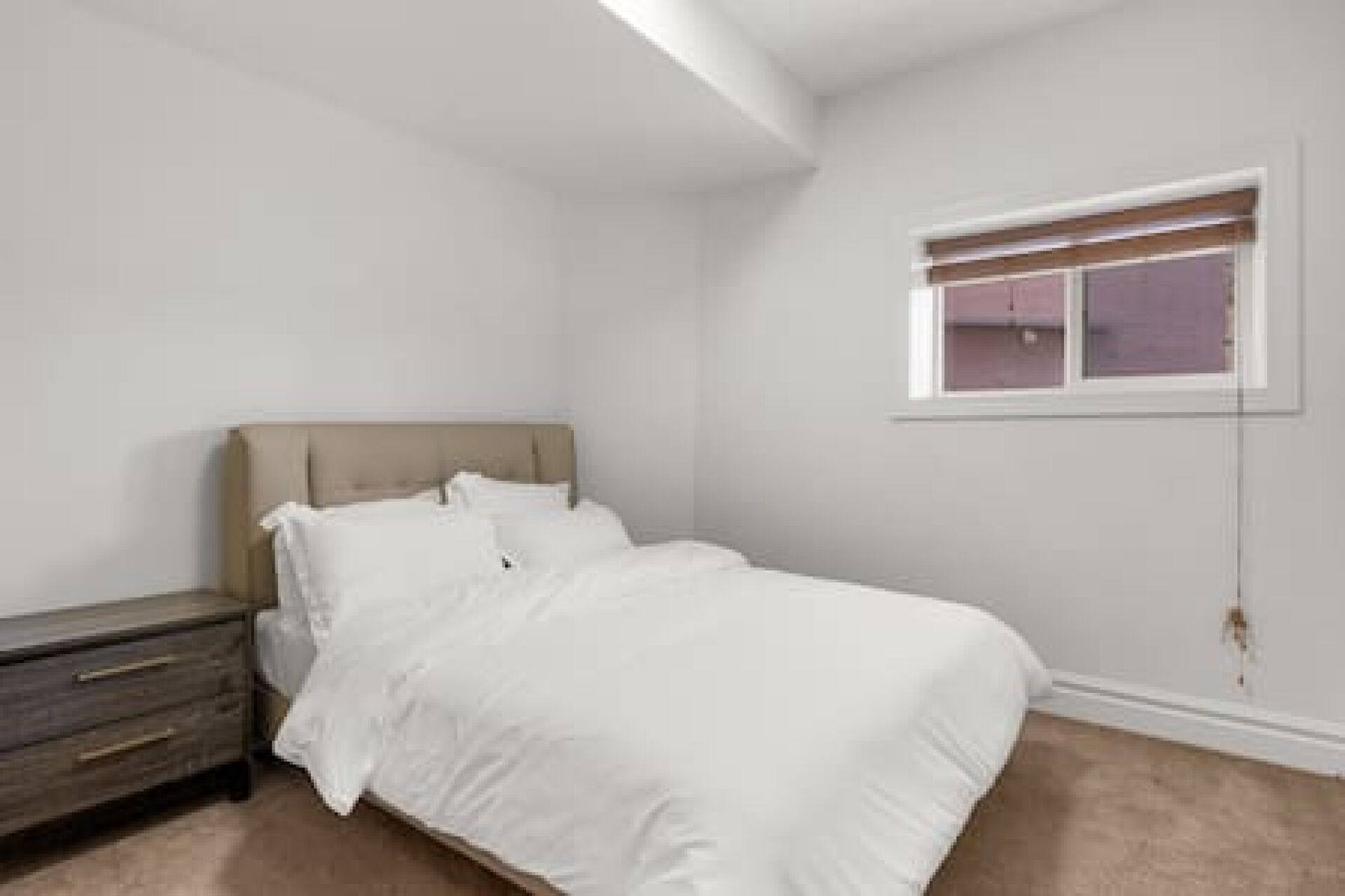 A bedroom with a bed, a nightstand, and a window.