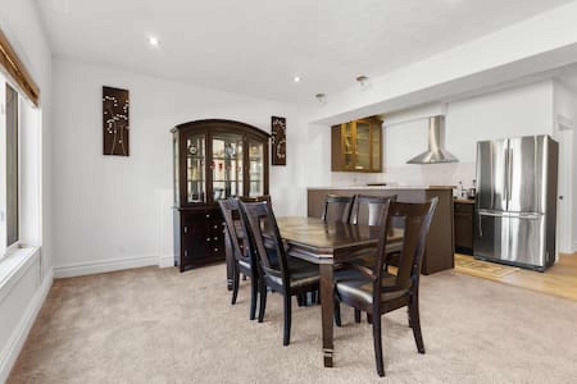 A dining area with a wooden table and chairs, a dark wooden cabinet, and a stainless steel refrigerator.