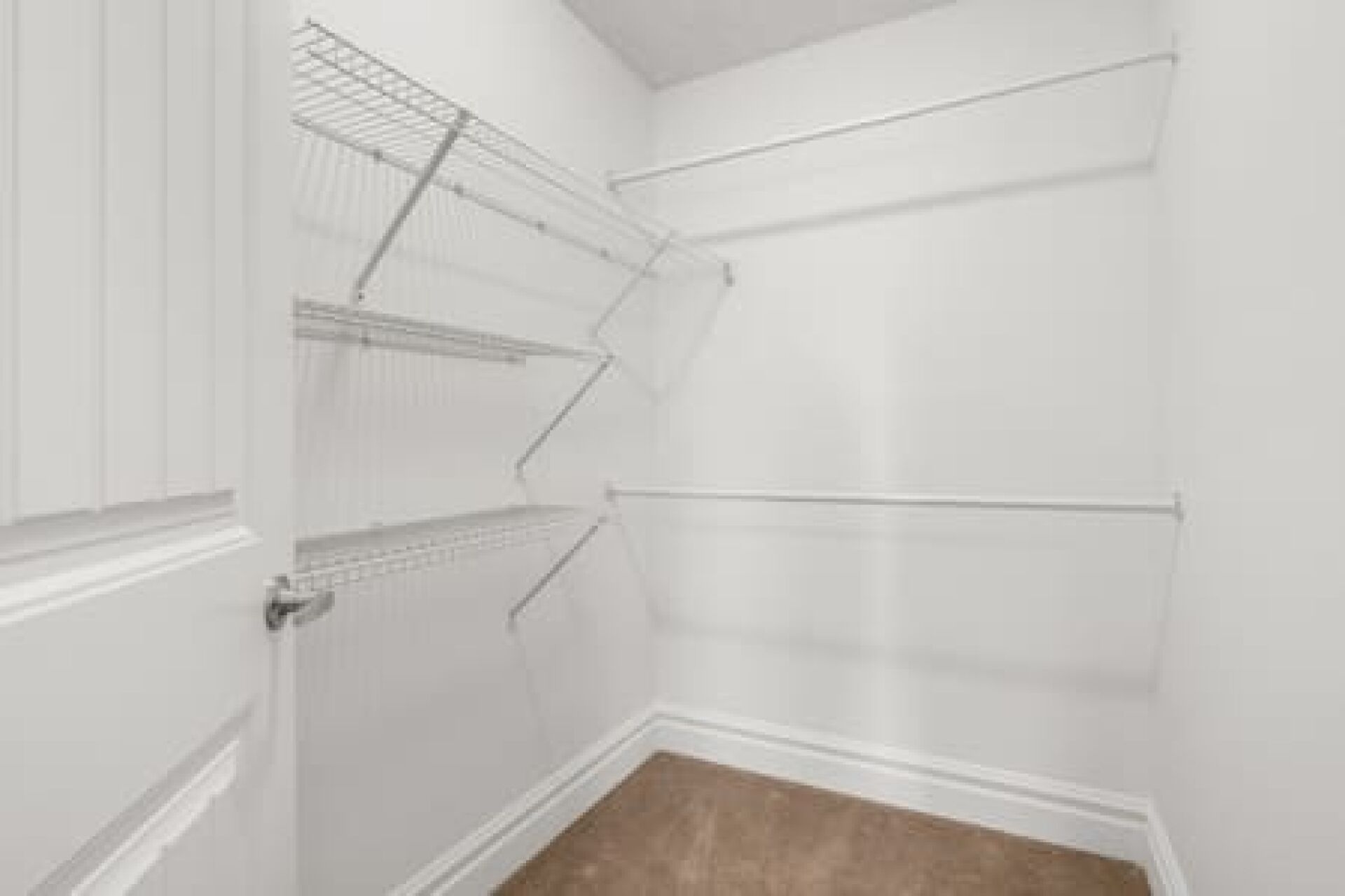 Un coin de pièce aux murs blancs, avec un plancher en bois et des étagères en fil de métal.