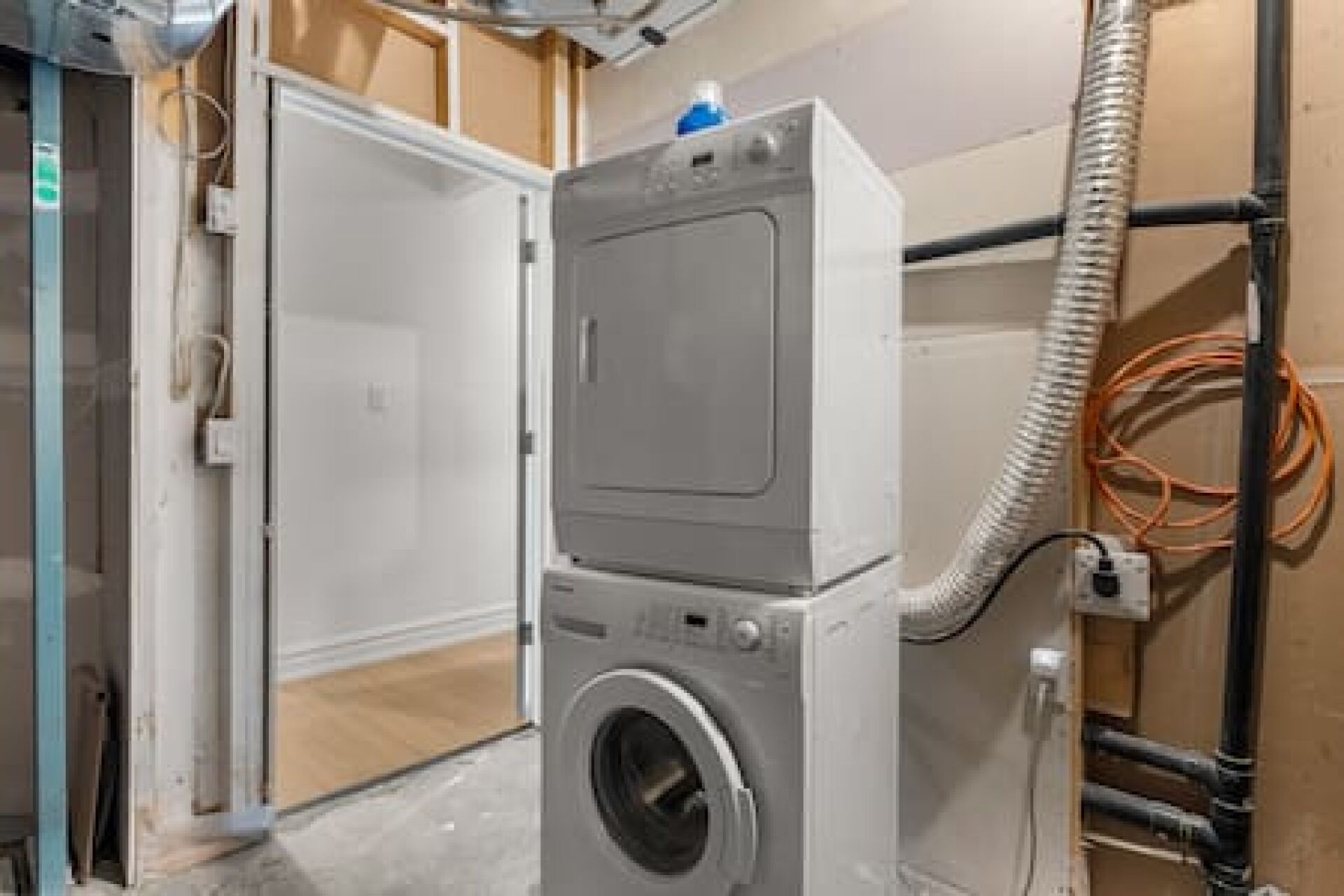 A compact, modern laundry room with a built-in washer and dryer, a visible electrical outlet, and a flexible hose.