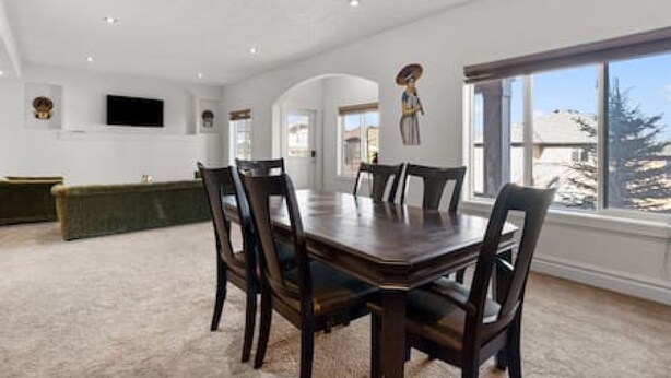 Un comedor con una mesa grande y sillas, un televisor en la pared y vistas al exterior.