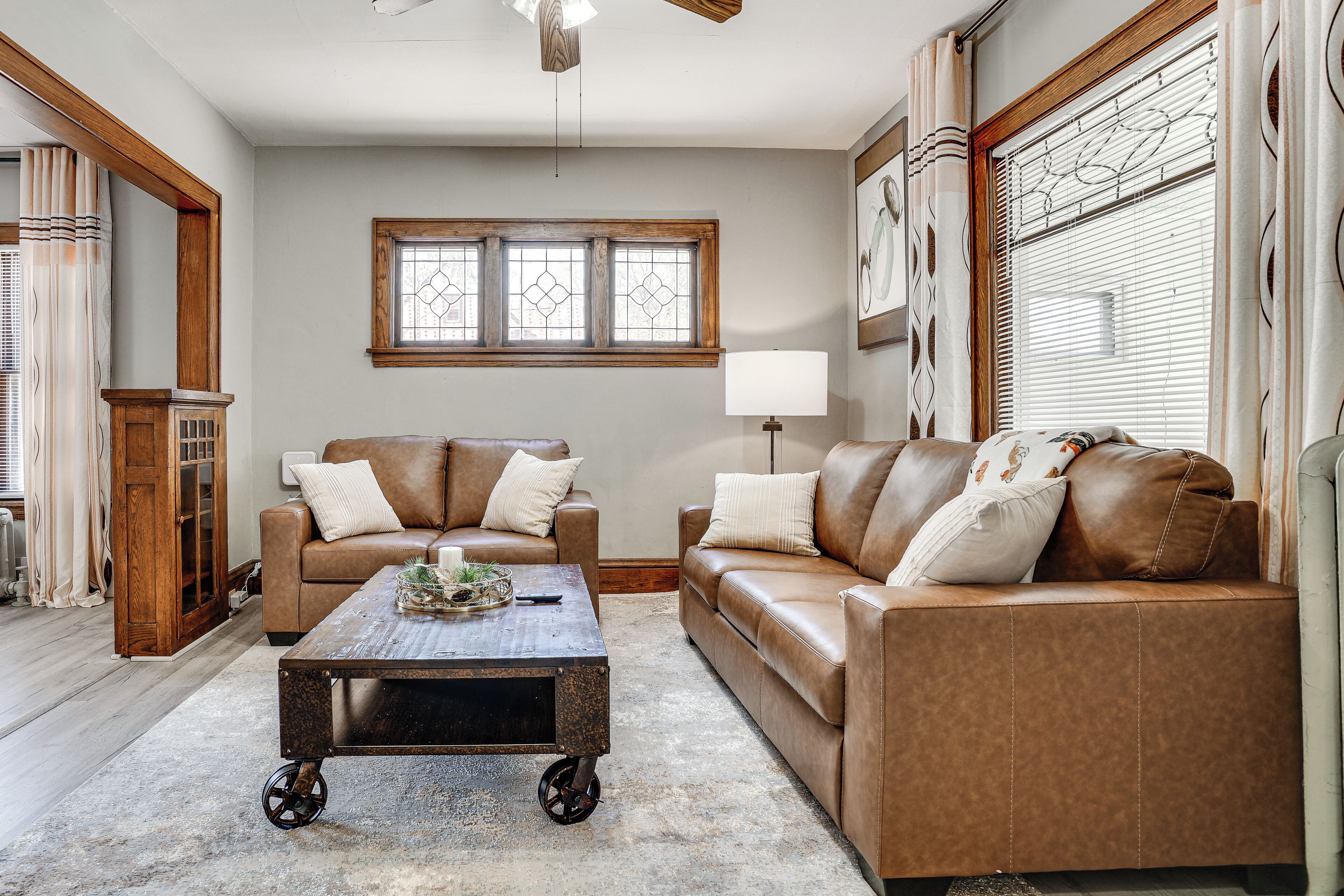 A living room with a brown leather sofa, a wooden coffee table, and a large window with blinds.