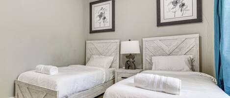 A room with two beds, a nightstand with a lamp, and two framed floral artworks on the wall.