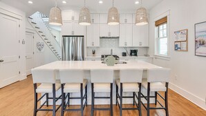 A modern kitchen with a large island, white cabinets, hanging pendant lights, and a staircase leading to another level. - Elegant Santa Rosa Beach House w/ Community Perks (Santa Rosa Beach)