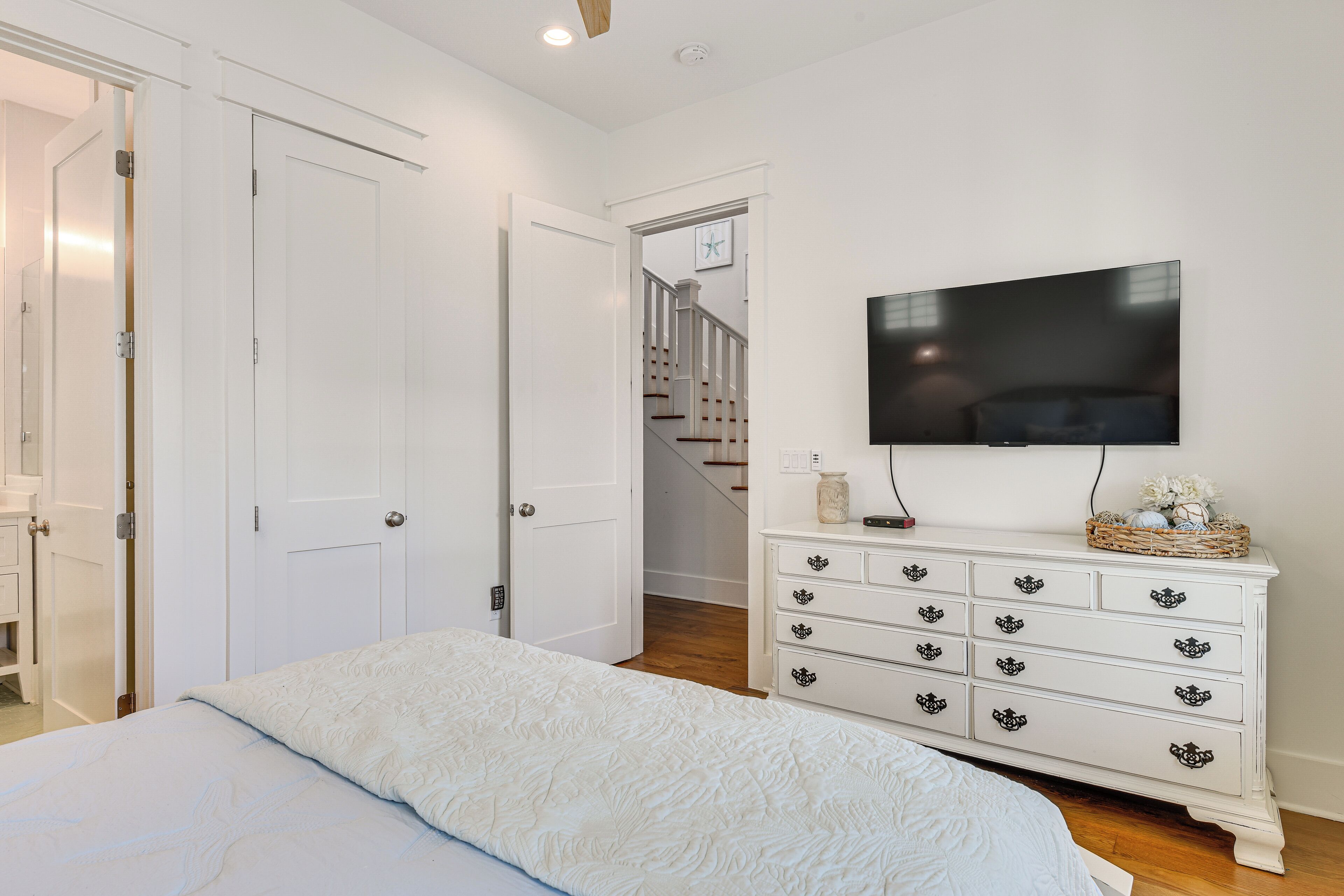 A bedroom with a bed, white dresser, television, and a staircase leading to another room.