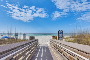 Ein hölzerner Steg führt zu einem Strand unter blauem Himmel.