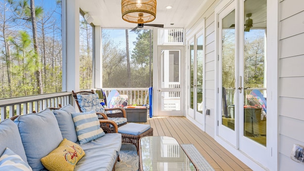 A covered porch with wicker furniture, a glass-top table, and a view of trees. - Elegant Santa Rosa Beach House w/ Community Perks (Santa Rosa Beach)