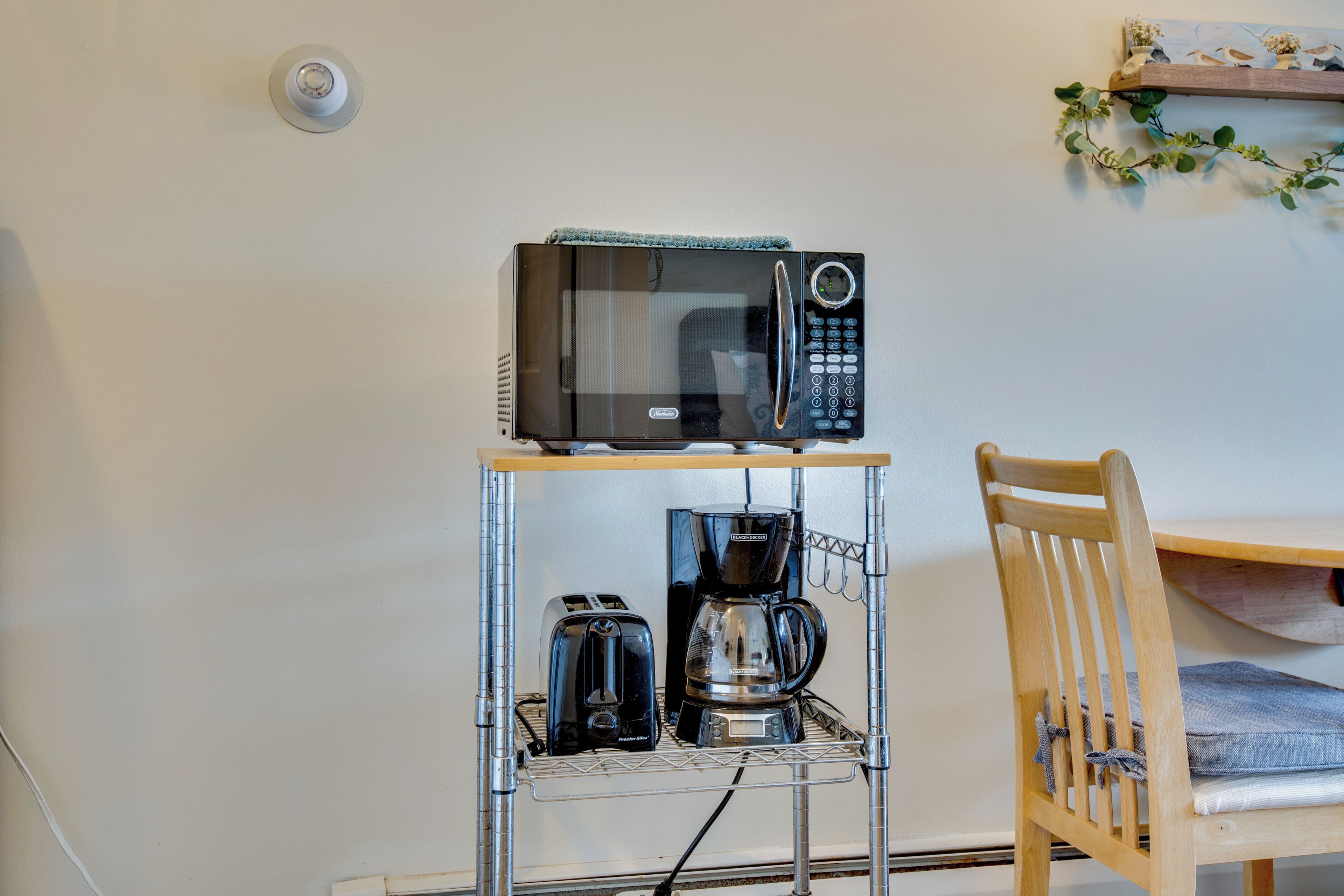 Zona cuina amb microones sobre un suport metàl·lic, torradora i cafetera.