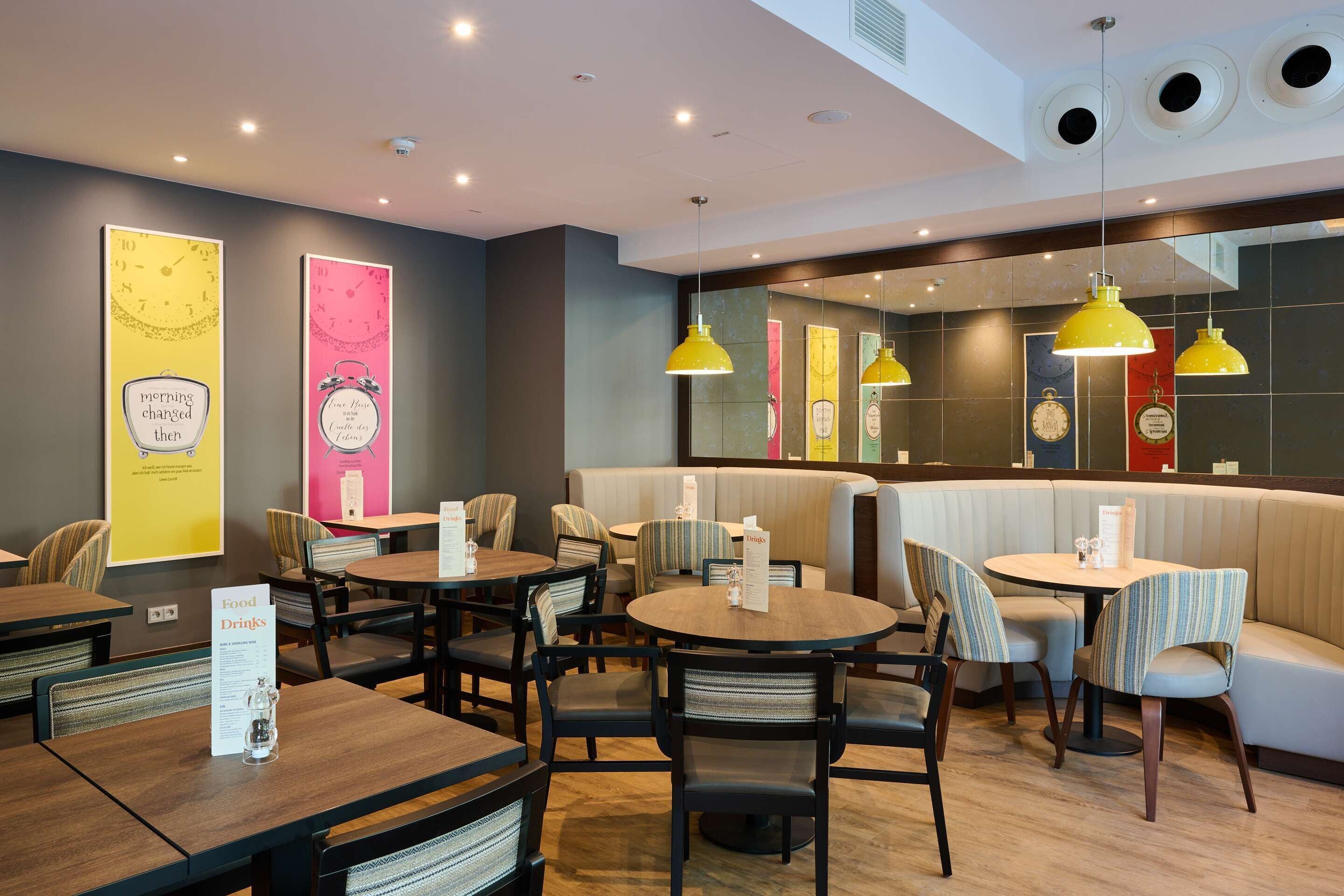 Un restaurant avec des tables rondes, des chaises à rayures et des lampes suspendues jaunes.