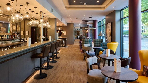A bar area with stools, a counter, and hanging light fixtures. - Premier Inn Frankfurt Eschborn (Eschborn)