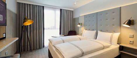 Quarto de hotel com uma cama grande, uma escrivaninha, uma cadeira, um abajur e vista para o exterior.