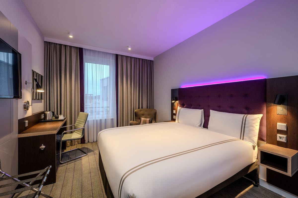 Habitación de hotel con una cama grande, un escritorio, una silla, un televisor y una ventana con cortinas.