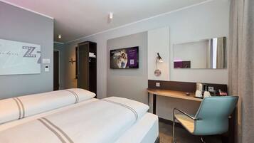 A hotel room with two beds, a desk, a chair, a TV, and a mirror.