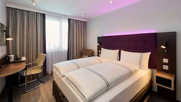 Una habitación de hotel con una cama grande, un escritorio con una silla, una mesita y una mesita de noche con una lámpara.