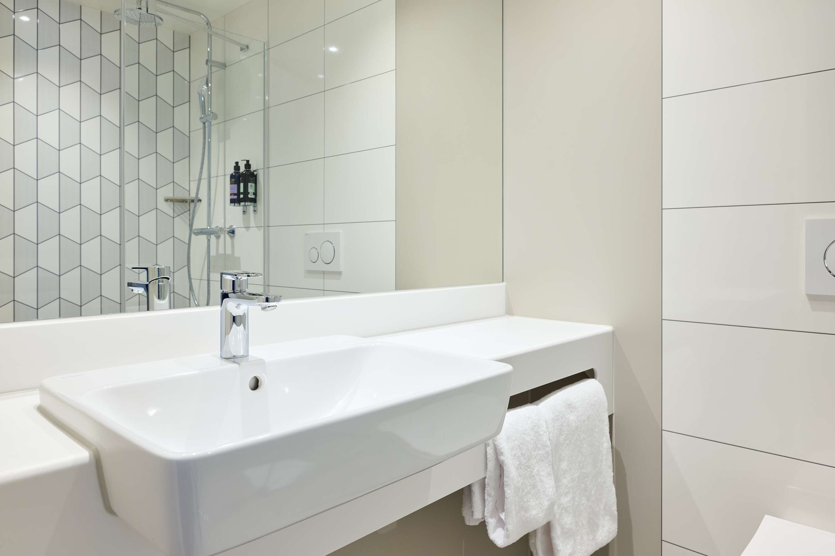 A modern bathroom with a large mirror, two sinks, and a shower.