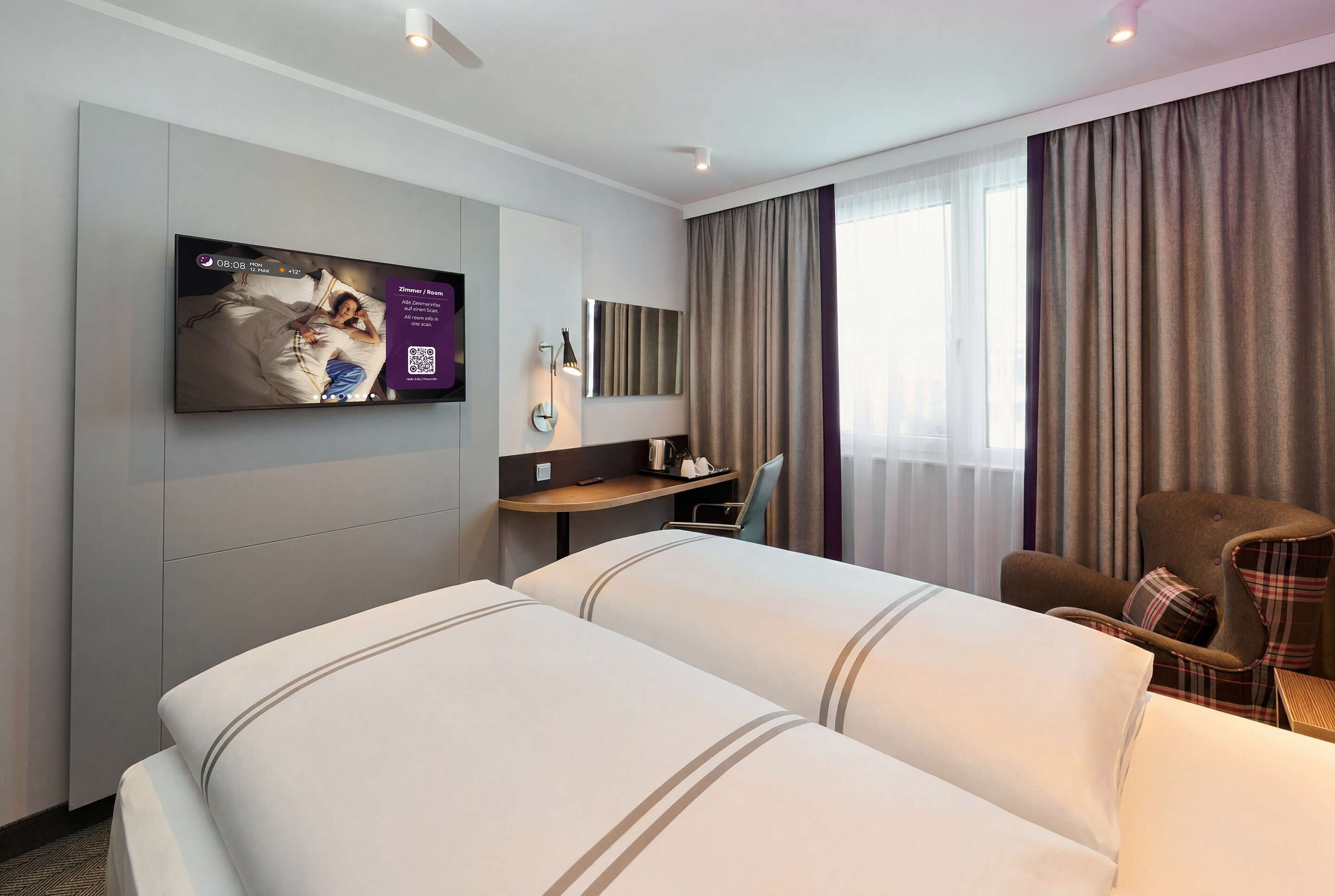 Habitación de hotel con dos camas, un televisor montado en la pared, un escritorio con una silla y un ventanal con cortinas.