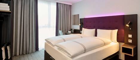 A hotel room with a large bed, a wardrobe, a nightstand, and a window with curtains.