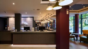 A modern reception area with a counter, seating, and large windows. - Premier Inn Frankfurt Eschborn (Eschborn)
