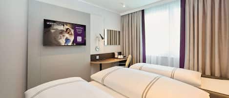 Une chambre d’hôtel avec deux lits, un téléviseur fixé au mur, un bureau avec une chaise et une grande fenêtre avec des rideaux.