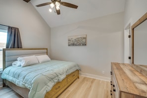 A bedroom with a bed, wooden dresser, ceiling fan, and a painting on the wall.