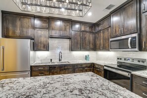 Una cocina moderna con armarios de madera oscura, un refrigerador de acero inoxidable, un microondas integrado y una amplia encimera de mármol.