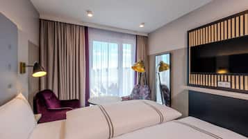 A hotel room with a bed, a chair, a small table, a TV, and a window with curtains.