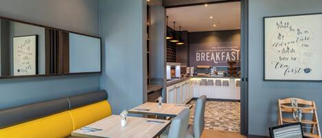 Un ristorante moderno con una colazione a buffet, un'area salotto e una cucina visibile sullo sfondo.