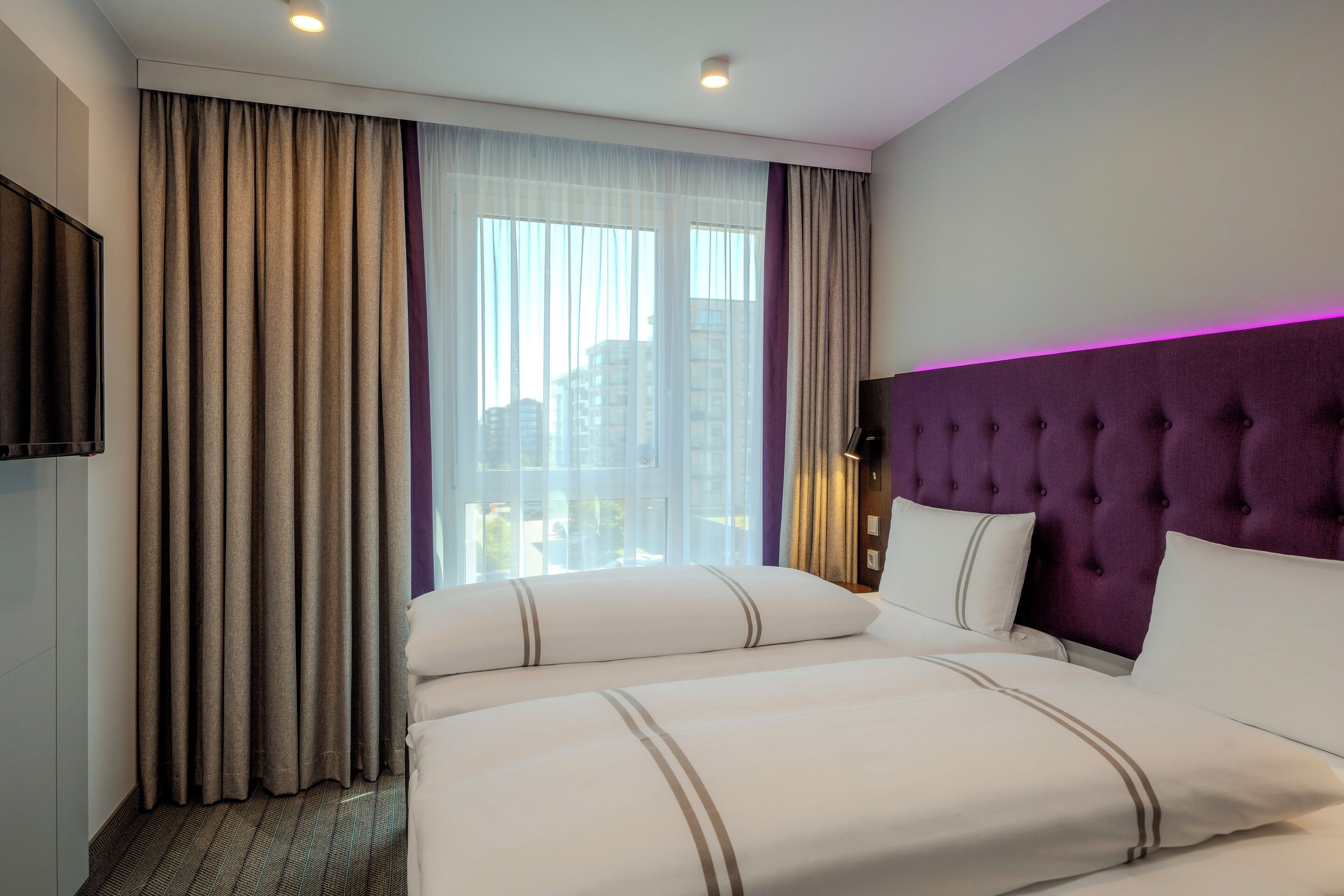 Habitación de hotel con una cama grande, televisión y vistas de la ciudad a través de la ventana.