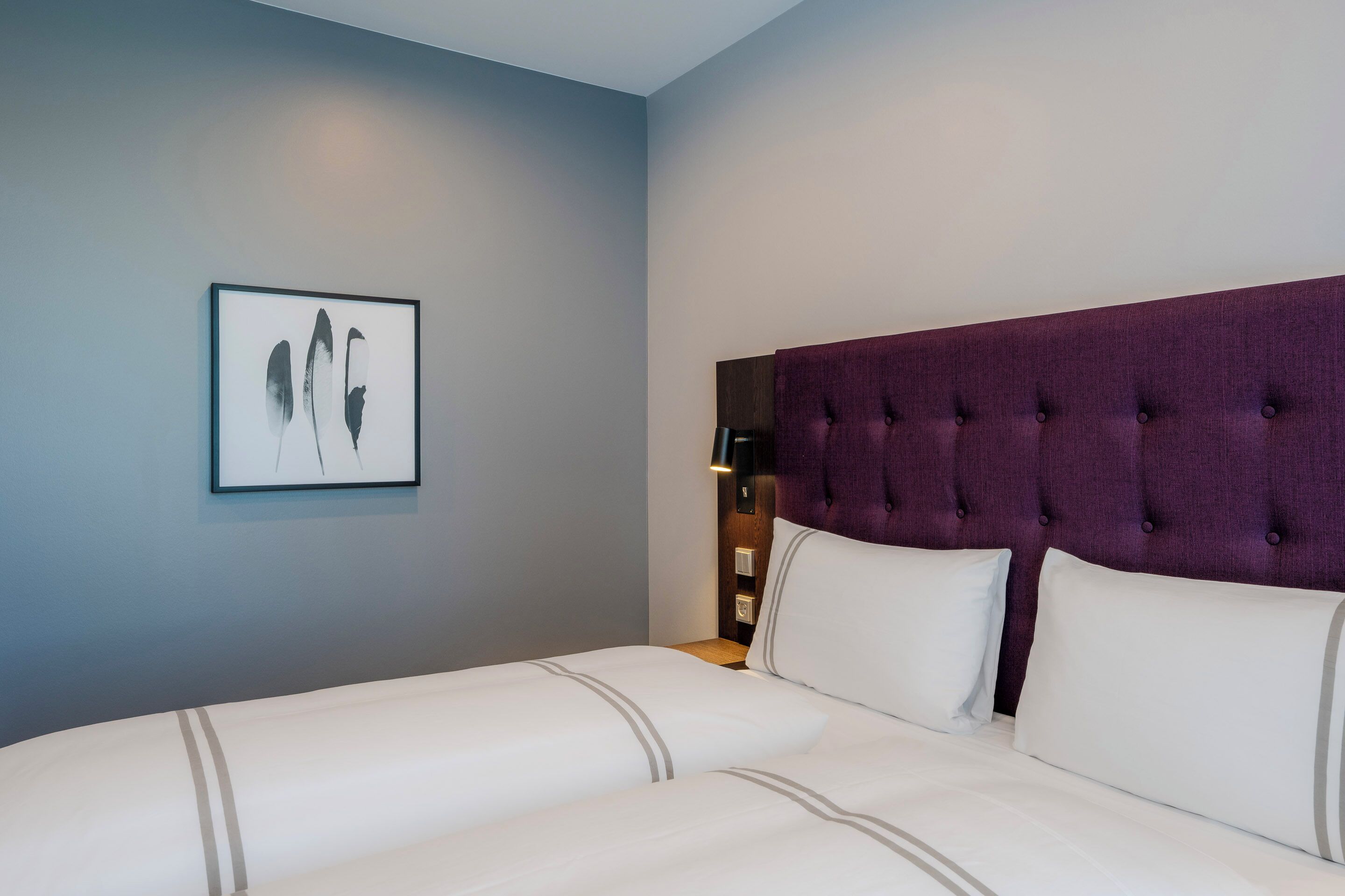 A hotel room with a large bed, a headboard, a nightstand, and a framed picture on the wall.