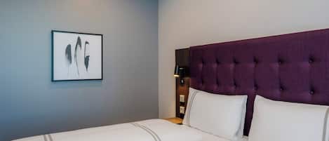 A hotel room with a large bed, a headboard, a nightstand, and a framed picture on the wall.