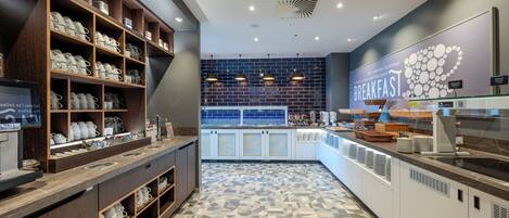 A breakfast area with shelves of mugs and cups, a counter with food items, and a wall with a breakfast sign.