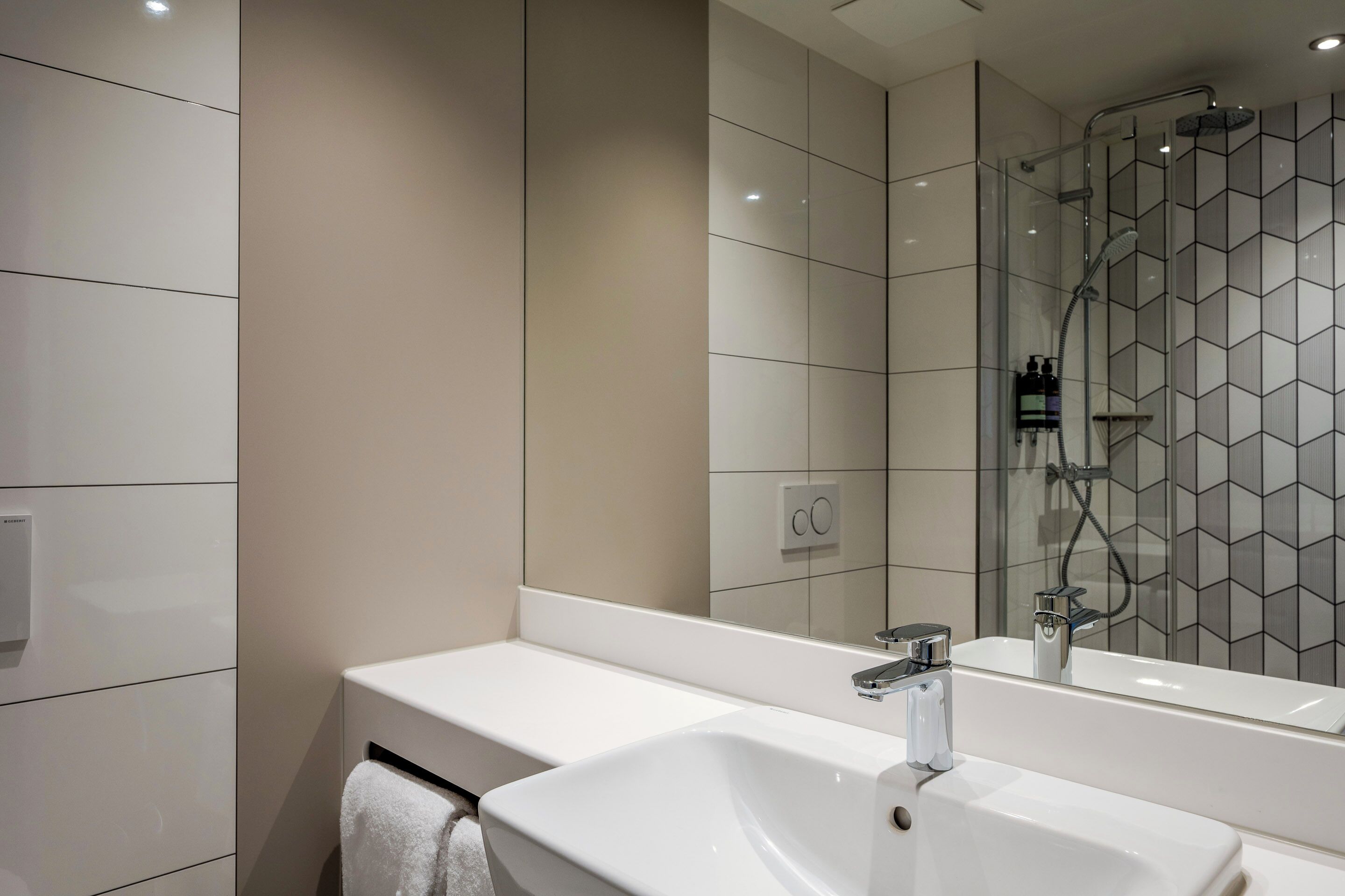 A modern bathroom with a white sink, a mirror, and a shower area.