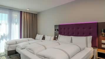 Une chambre d’hôtel avec deux lits, une grande fenêtre avec des rideaux, une tête de lit violette et une table de chevet.