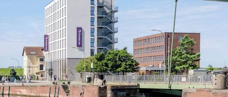 Un bâtiment moderne, facilement reconnaissable à son grand panneau « Premier Inn », une structure en briques surmontée d’un toit végétalisé, et un canal traversé par un pont.