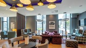 A modern lounge area with sofas, chairs, and tables, large windows, and ceiling lights.