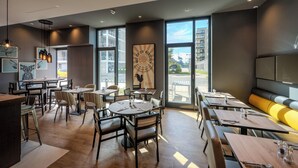 A modern restaurant interior with round tables, chairs, and a large window offering a city view.