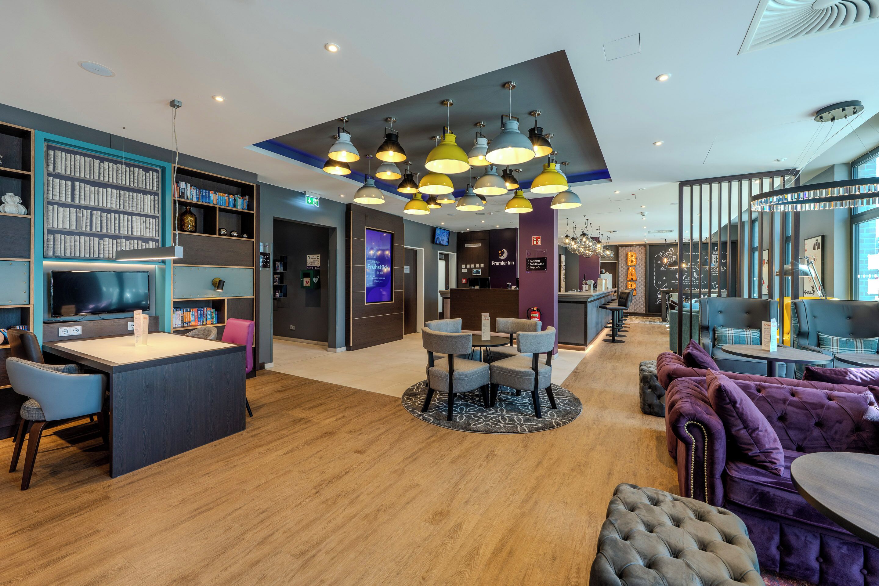 En modern hotellobby med en central sittgrupp, en bar och en bokhylla.