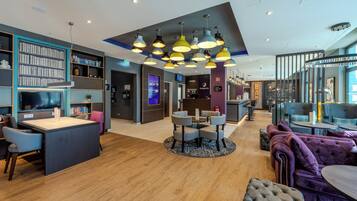En modern hotellobby med en central sittgrupp, en bar och en bokhylla.