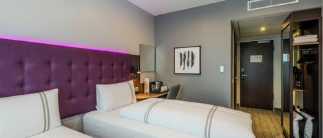 A hotel room with two beds, a purple headboard, a desk with a chair, a mirror, and a wardrobe.