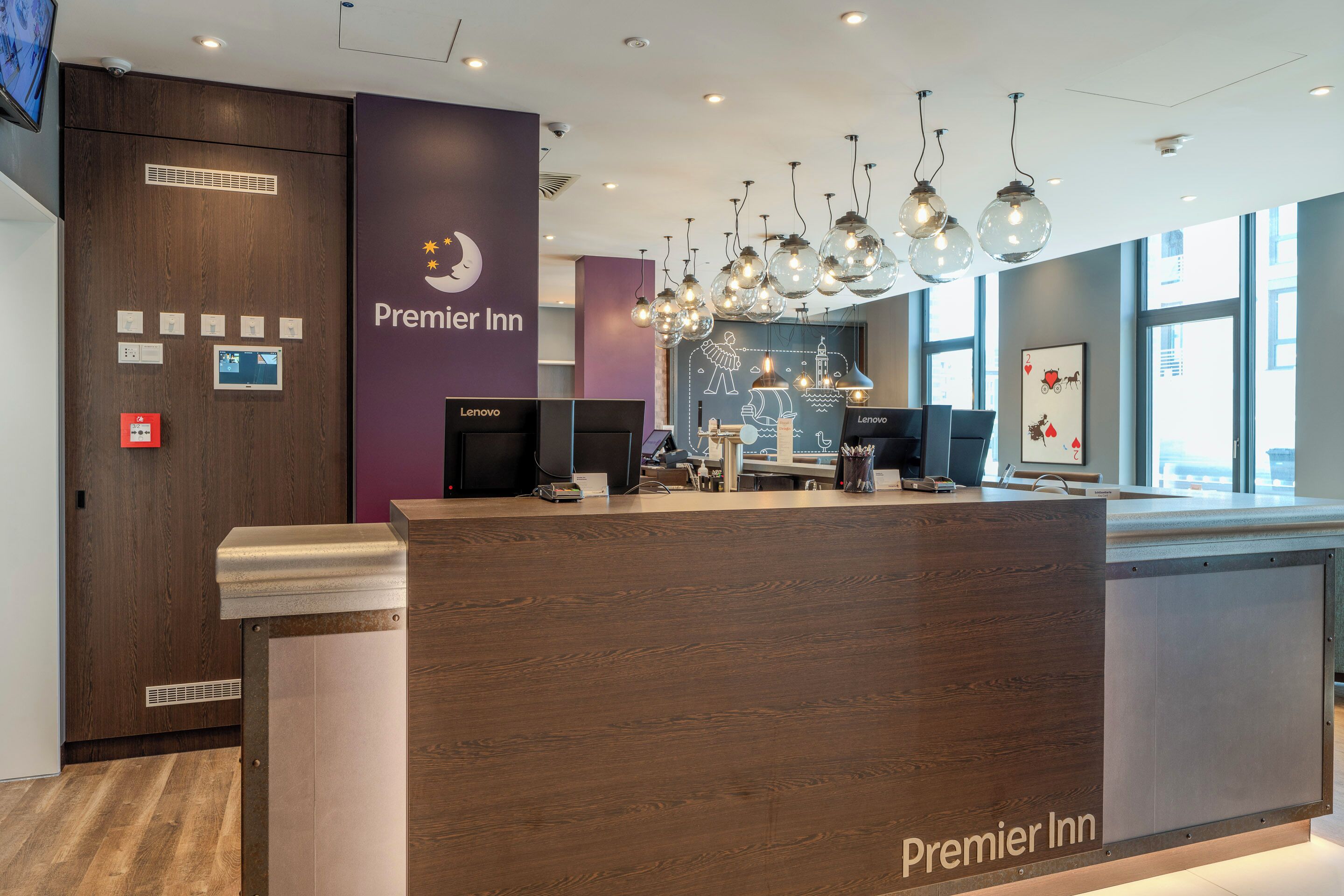 Een receptiebalie van een 'Premier Inn' hotel, met een digitaal scherm en een bureau met een computer.