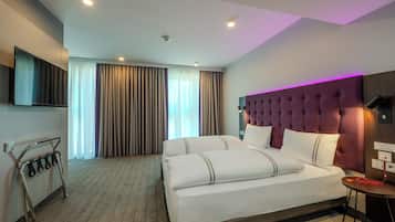 A hotel room with a large bed, a headboard with a tufted design, a flat-screen TV mounted on the wall, and a small table with a lamp.