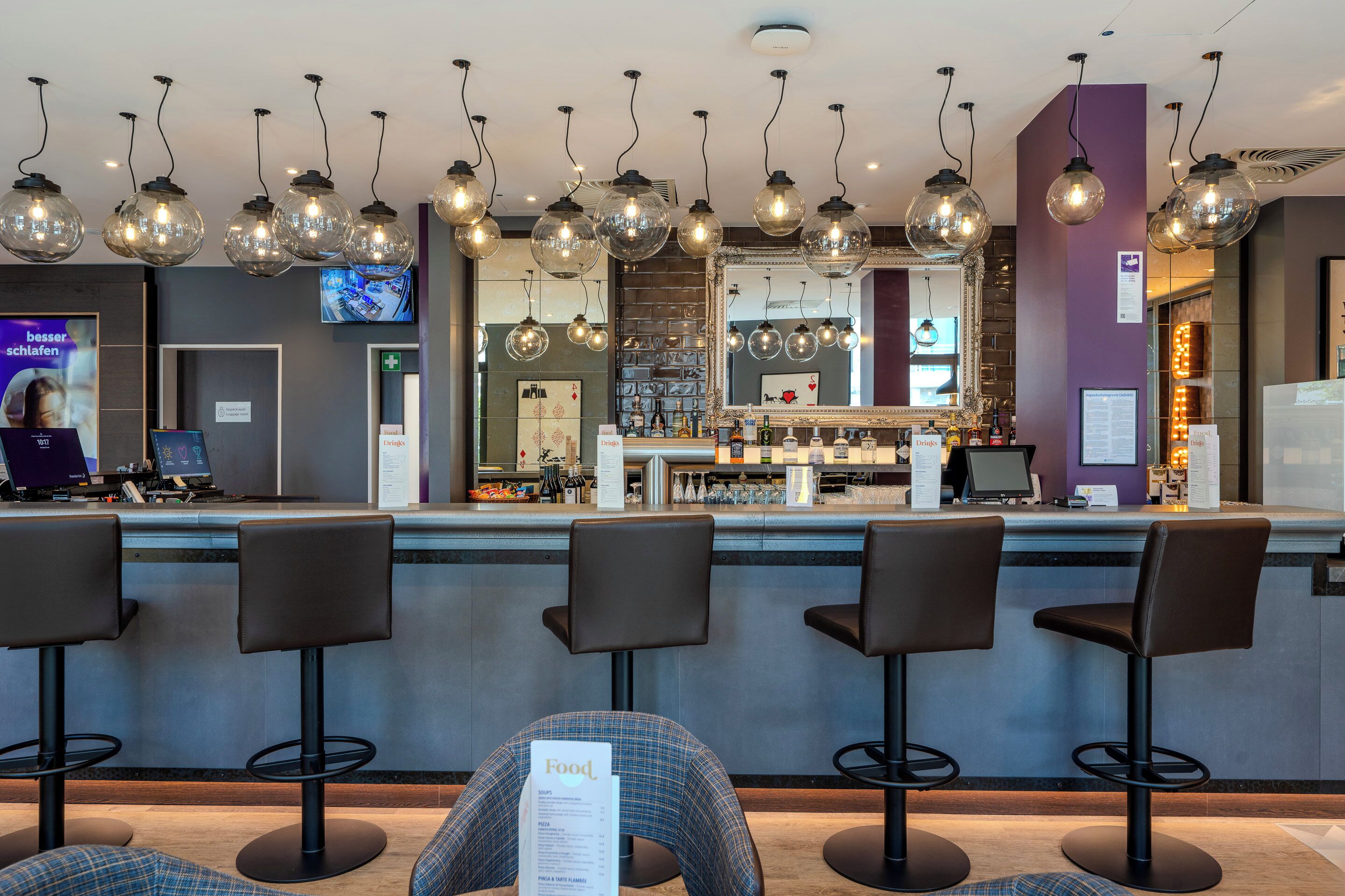 Zona de bar con varios taburetes, una barra con menú e iluminación colgante.