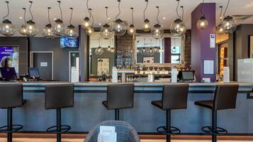 Zona de bar con varios taburetes, una barra con menú e iluminación colgante.
