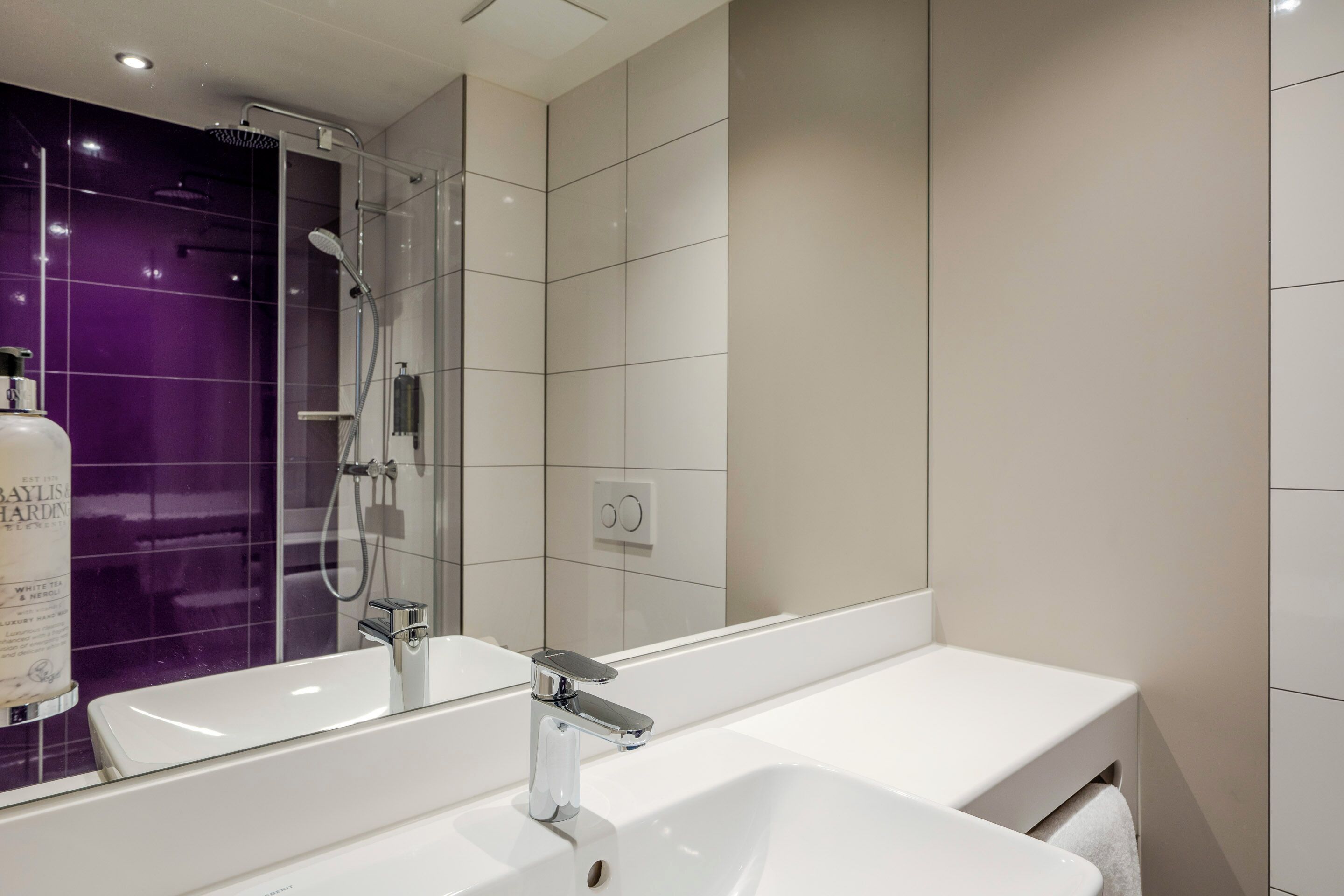 A modern bathroom with a large mirror, a white sink, and a shower area.