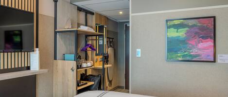 A hotel room with a bed, a wardrobe, a desk, and a painting on the wall.