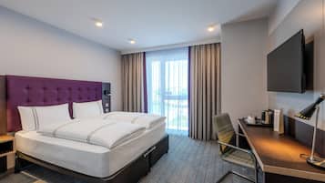 A hotel room with a large bed, a desk with a chair, a flat-screen TV, and a window with curtains.