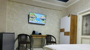 A hotel room with a bed, a TV mounted on the wall, a small table with chairs, a refrigerator, and a patterned rug. - ALI HOTEL (Namangan)